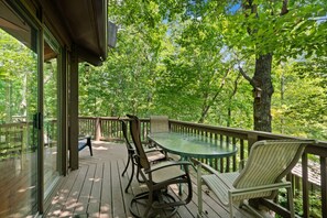 A wooden deck with a glass table and chairs, surrounded by lush greenery and trees. - Treetopper Knoll Chalet in Big Canoe (Jasper)