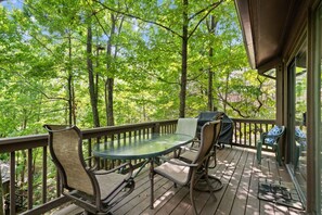 A wooden deck with a glass table and chairs, surrounded by trees. - Treetopper Knoll Chalet in Big Canoe (Jasper)