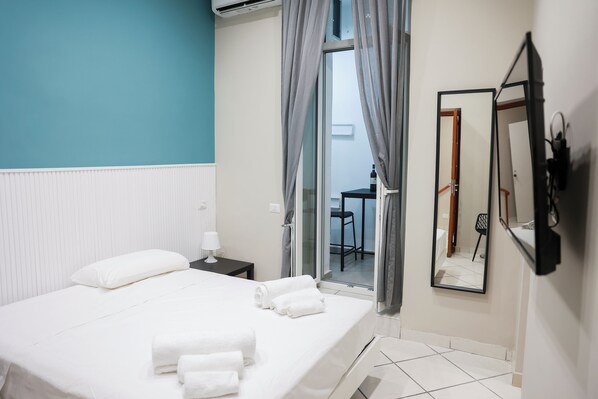 Une chambre d’hôtel comprenant un lit, une table de chevet, un miroir et une porte-fenêtre coulissante donnant sur un balcon.