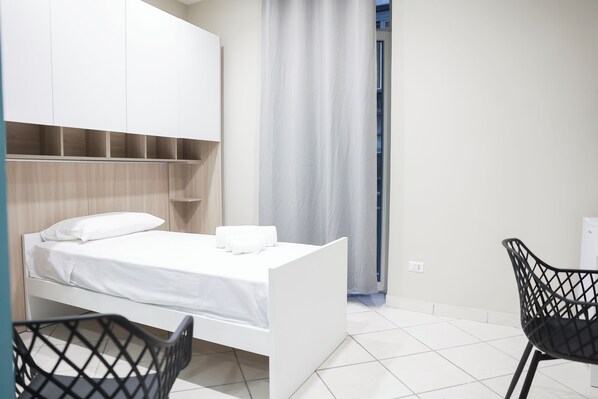 Une chambre à coucher moderne avec un lit blanc, une armoire et une chaise noire.