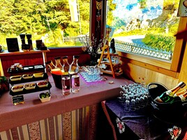 Una mesa con diversos alimentos y bebidas, una escalera y una vista de vegetación al exterior.