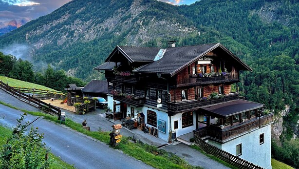 Un chalet traditionnel en bois, doté d’un balcon, situé dans un cadre montagneux.