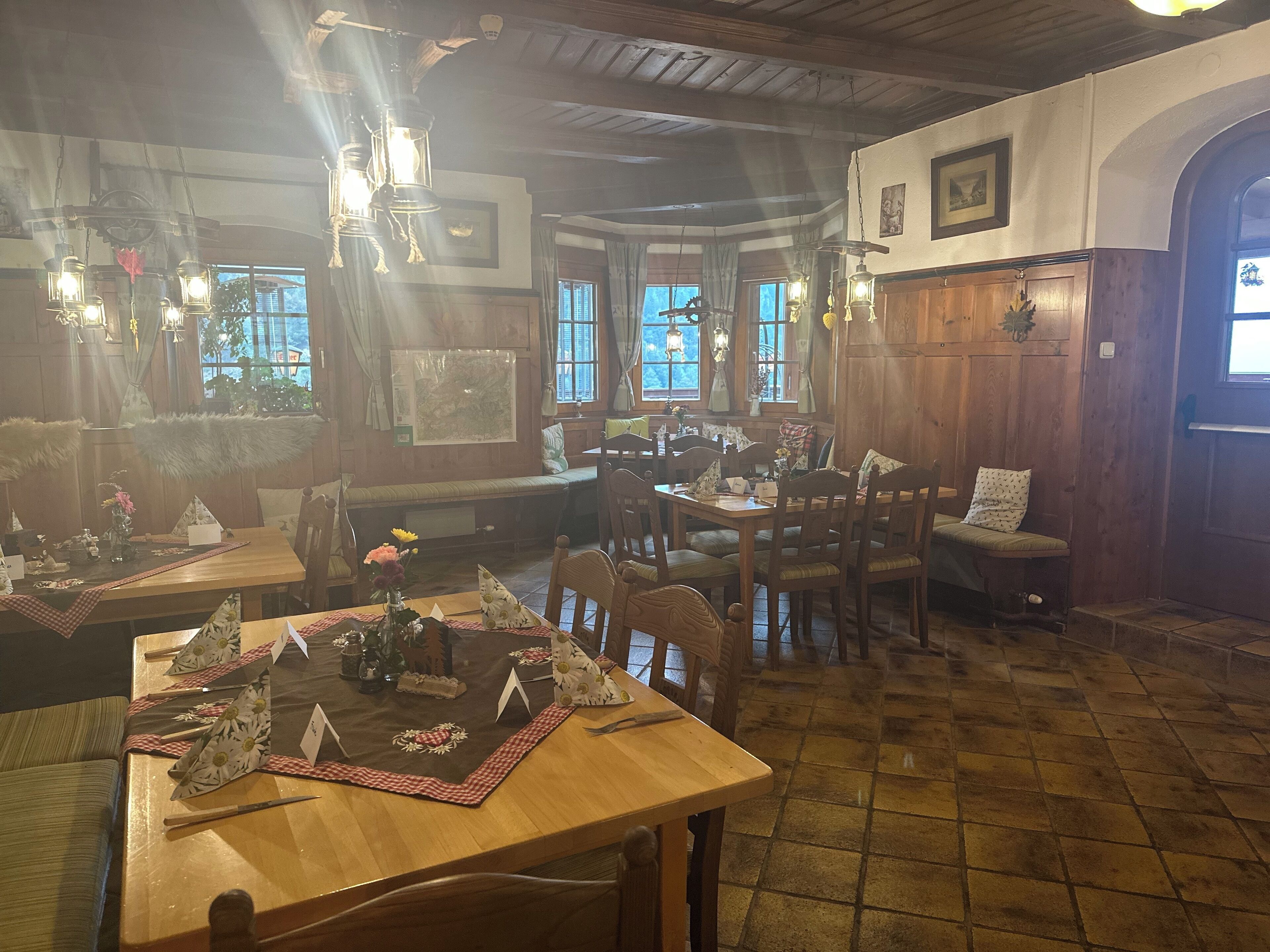 Interior acogedor de un restaurante con paredes de madera, un techo alto y faroles colgantes. Las mesas están preparadas con manteles individuales y centros de mesa.