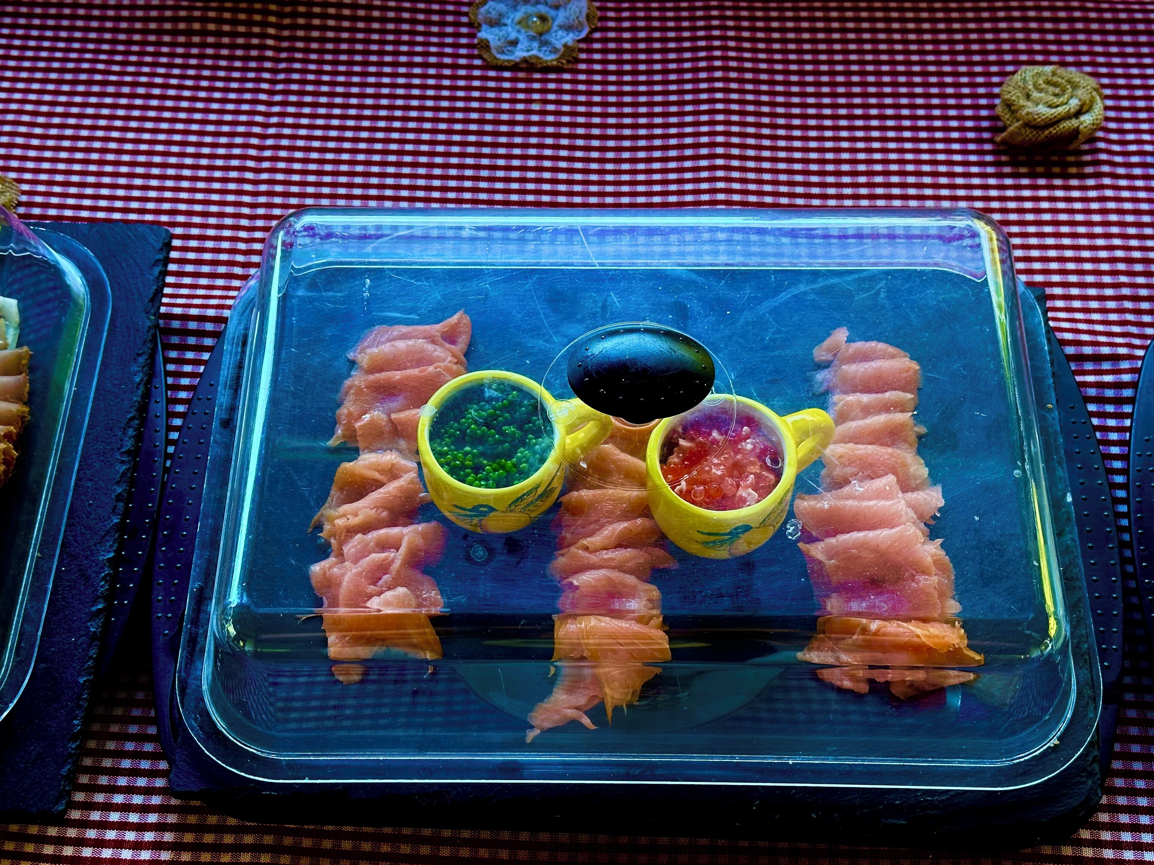 Un plateau de service en verre, sur lequel on trouve du saumon et deux sauces colorées, le tout posé sur une nappe à carreaux rouges et blancs.
