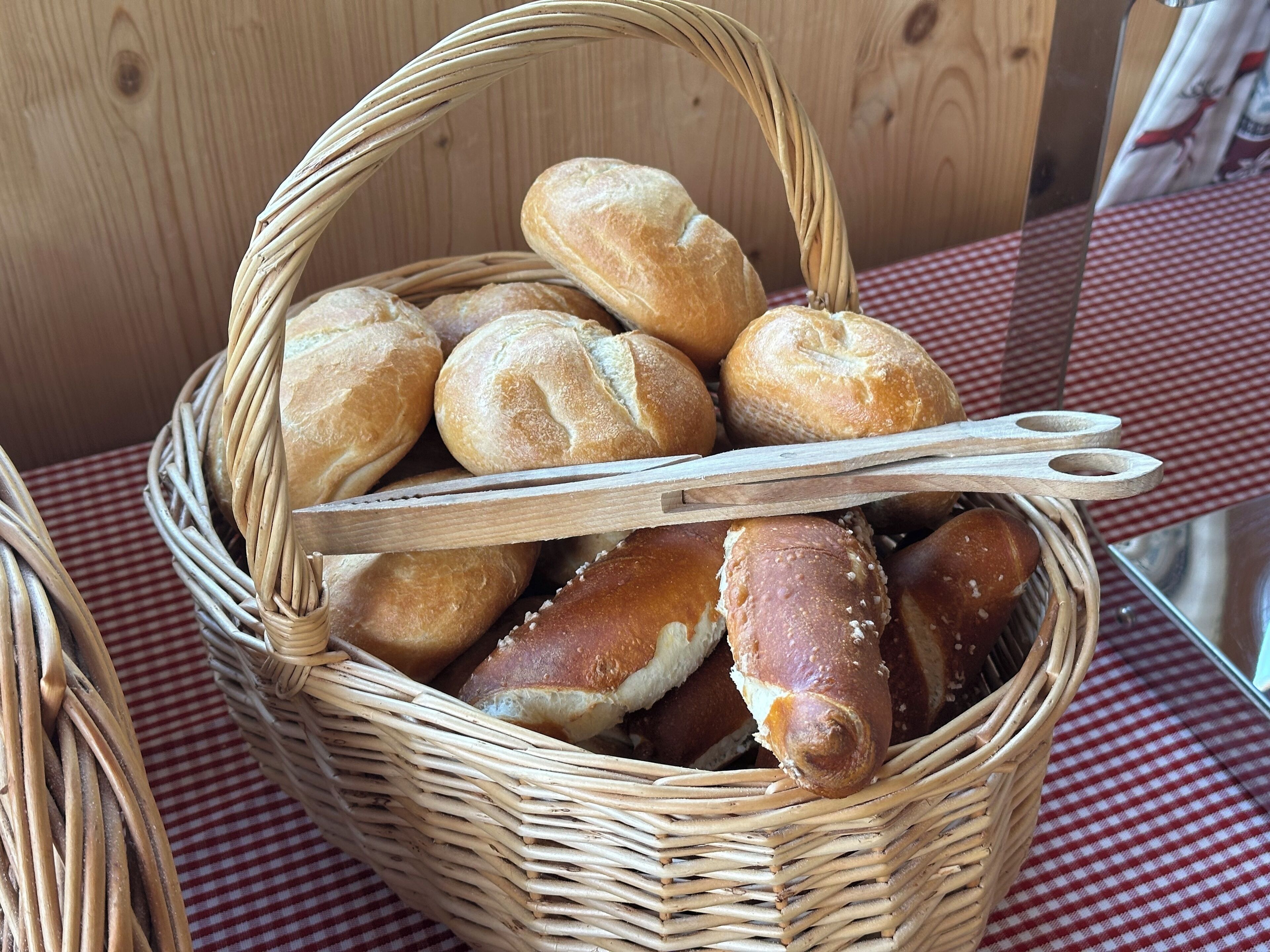 Un panier en osier rempli de différents types de pain, posé sur une nappe à carreaux.
