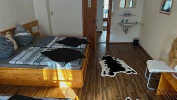 Un dormitorio con una cama de madera, una silla blanca, un tapiz de cuero de vaca y un baño con lavamanos y espejo.