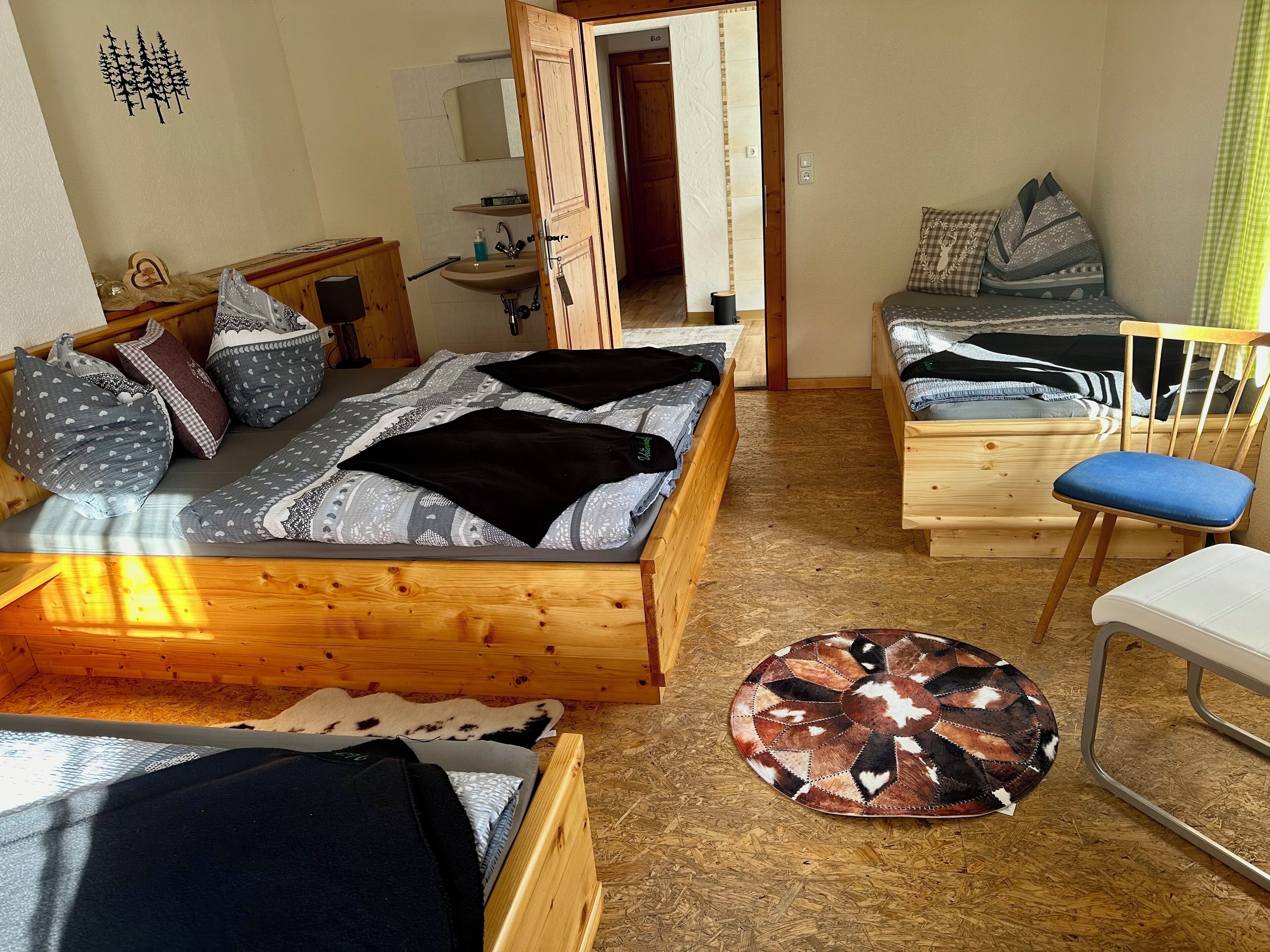 Una habitación pequeña con una cama de madera, un escritorio, una silla y un tapete redondo.