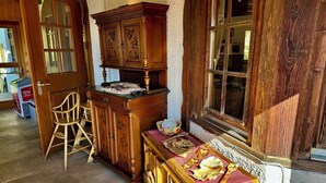 Une pièce au décor traditionnel, avec un buffet en bois, une petite table en bois recouverte d’une nappe à carreaux et une chaise.