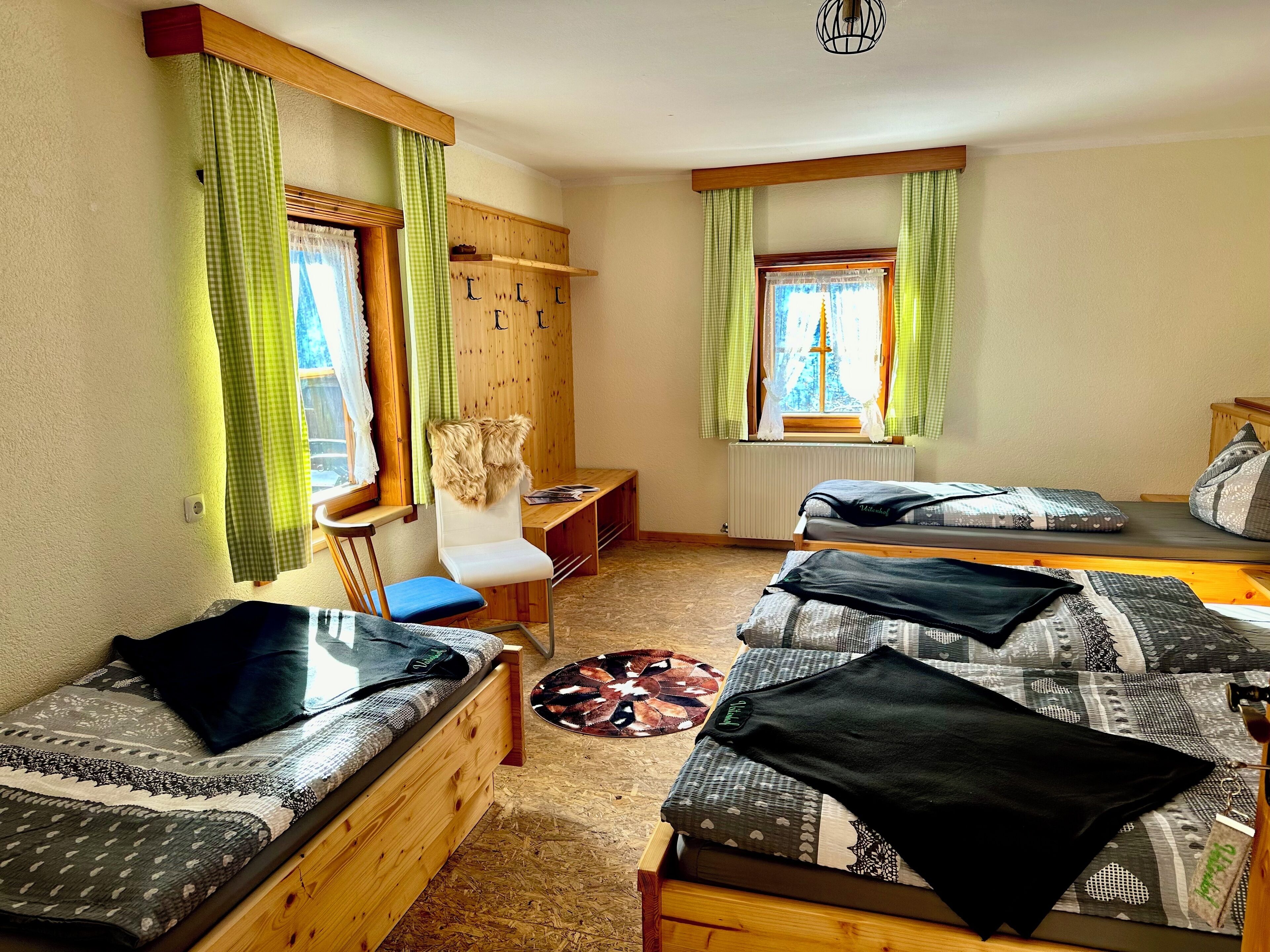 Una habitación acogedora con dos camas de madera, una silla, una mesita y una ventana con cortinas.
