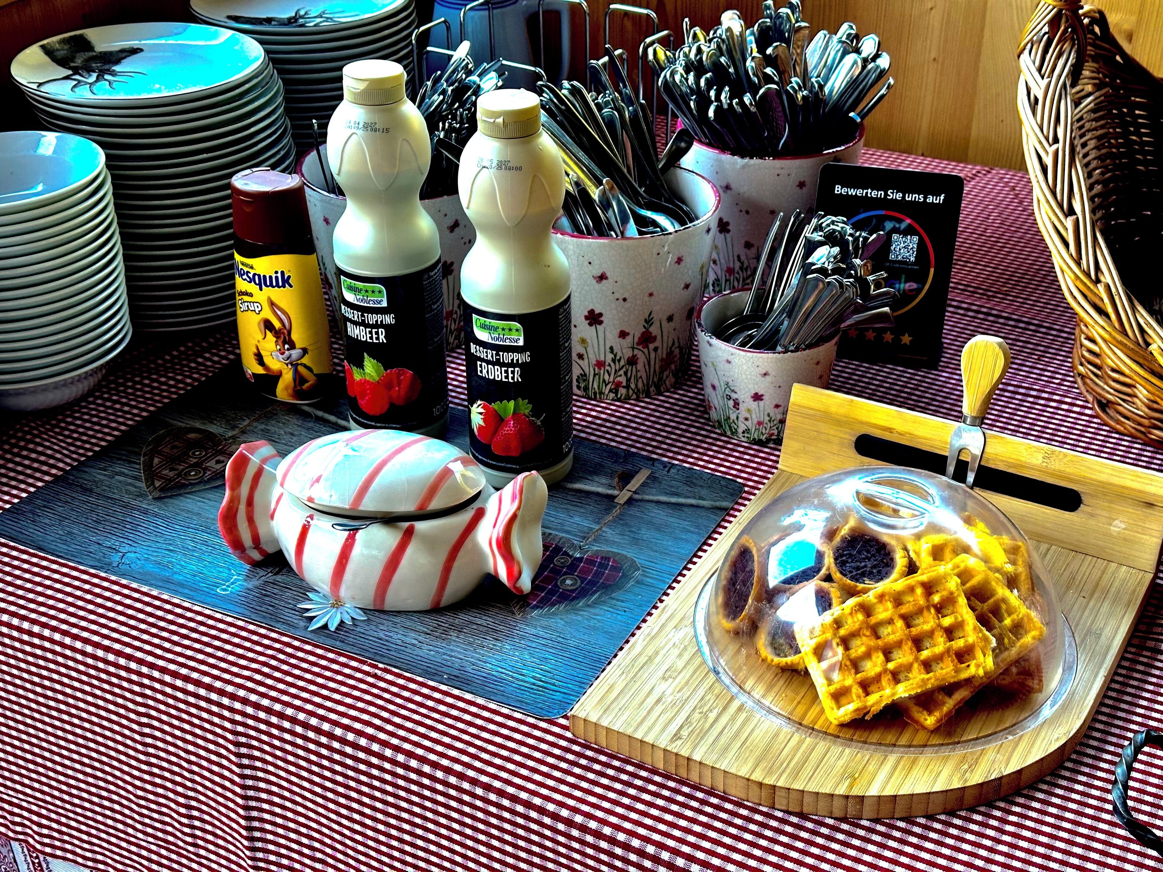 A table with plates, utensils, bottles, and a waffle.