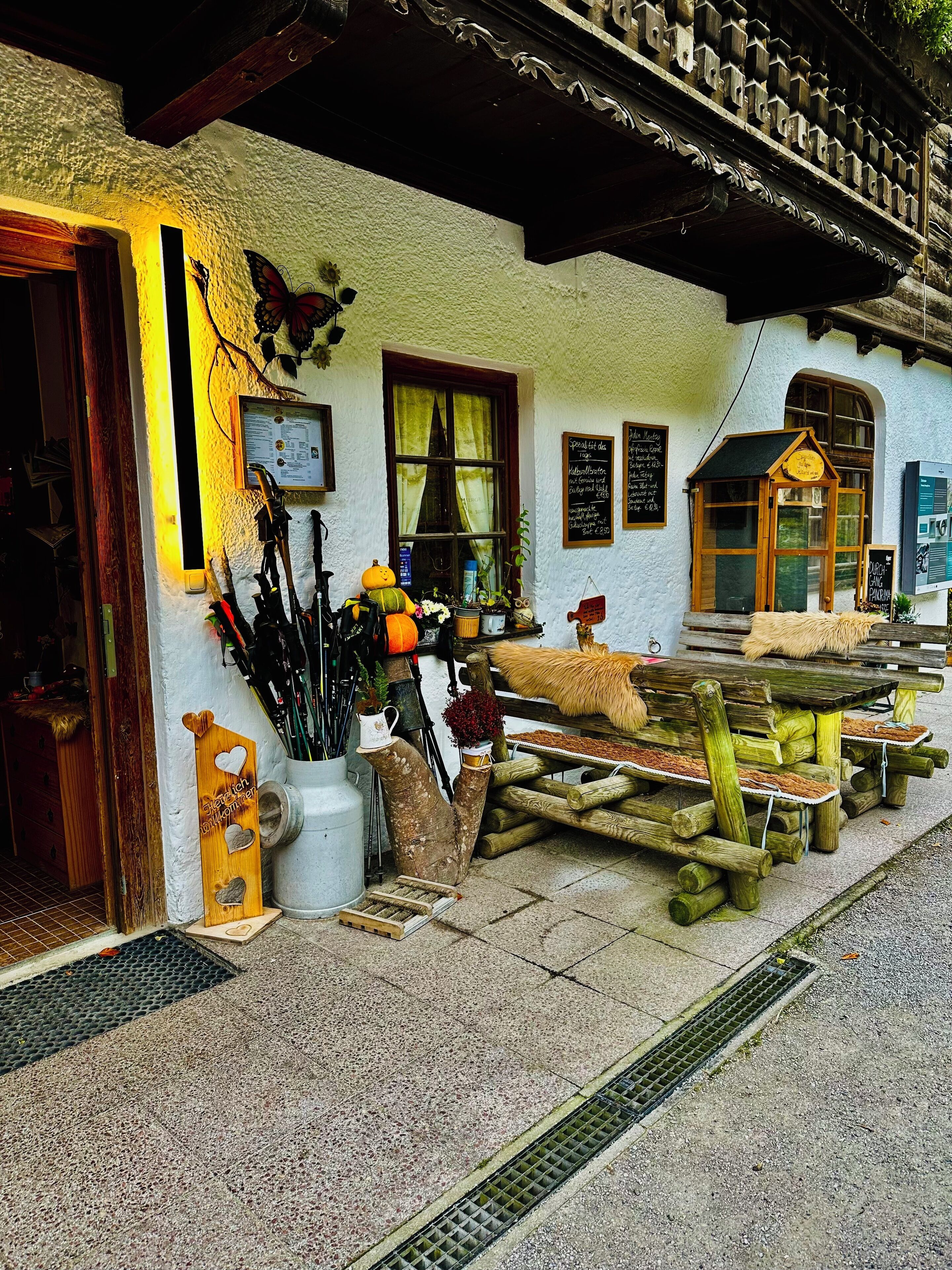 A rustic building with a wooden bench outside, a signboard, and a window with curtains.