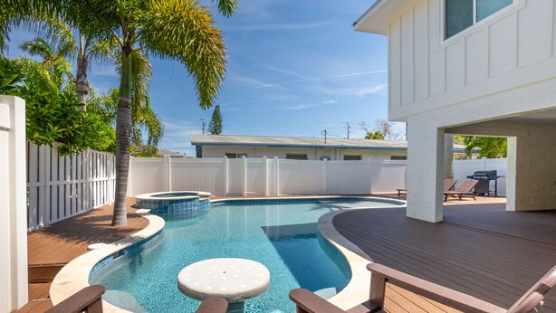 Ein Swimmingpool mit Holzterrasse, Liegestühlen und einer Palme.