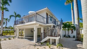 Ein Strandgrundstück mit zwei Etagen, einem Balkon, Palmen und einer Sandauffahrt.