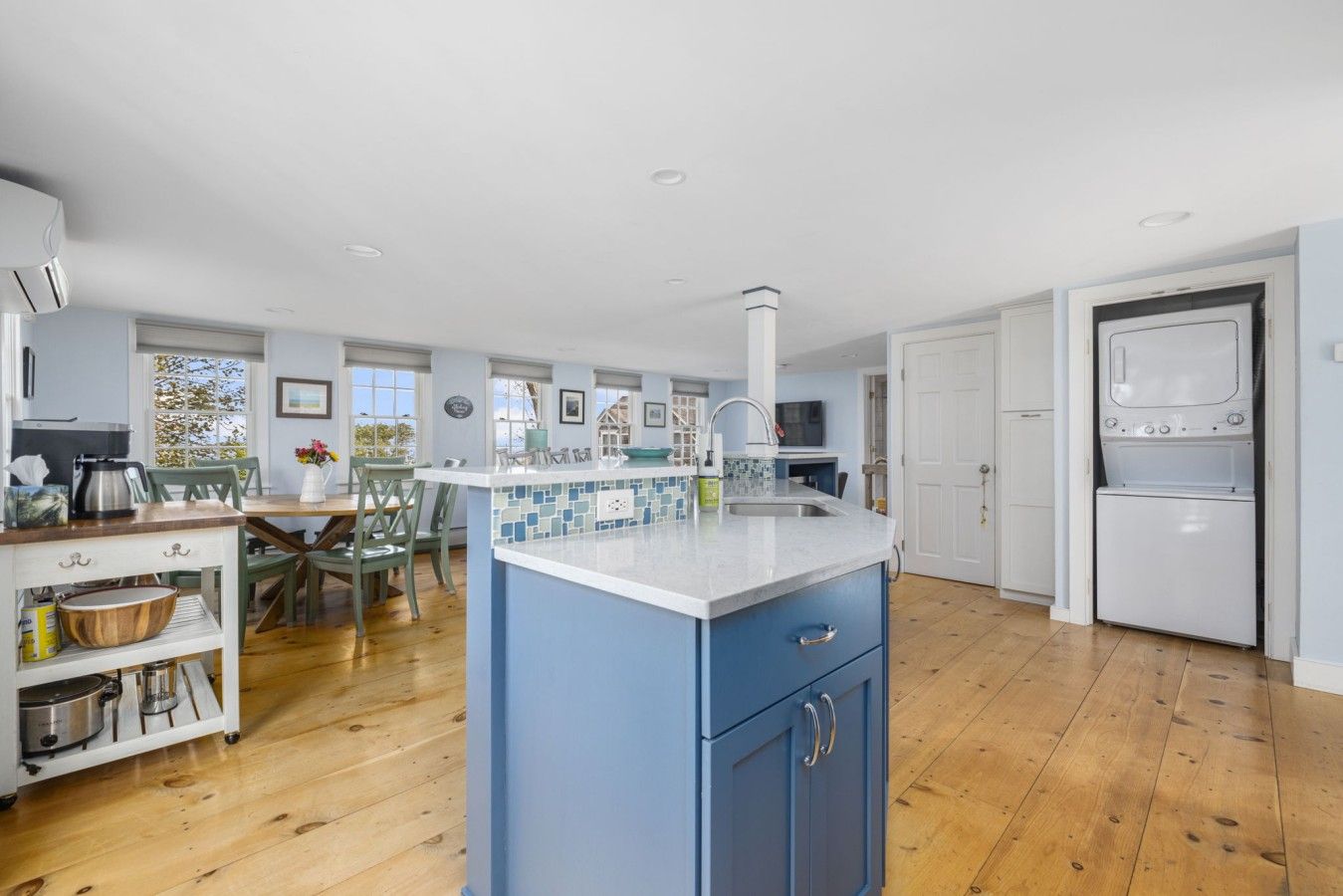 A spacious kitchen with a central island, wooden flooring, and a view of the outdoors.