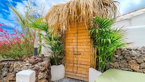 A wooden door with a thatched roof, surrounded by plants and a stone wall.