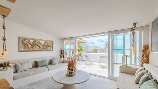 A modern living room with a sofa, a coffee table, and a view of the ocean through large sliding doors.