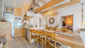 A modern kitchen with wooden cabinetry, a central island with chairs, and a dining area with a chandelier.