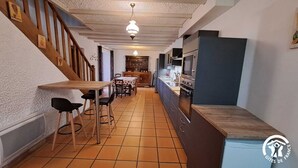A narrow kitchen with a wooden table and chairs, a built-in oven, and a TV. - Fraissines at Myriam and Laurent's (FRAISSINES)