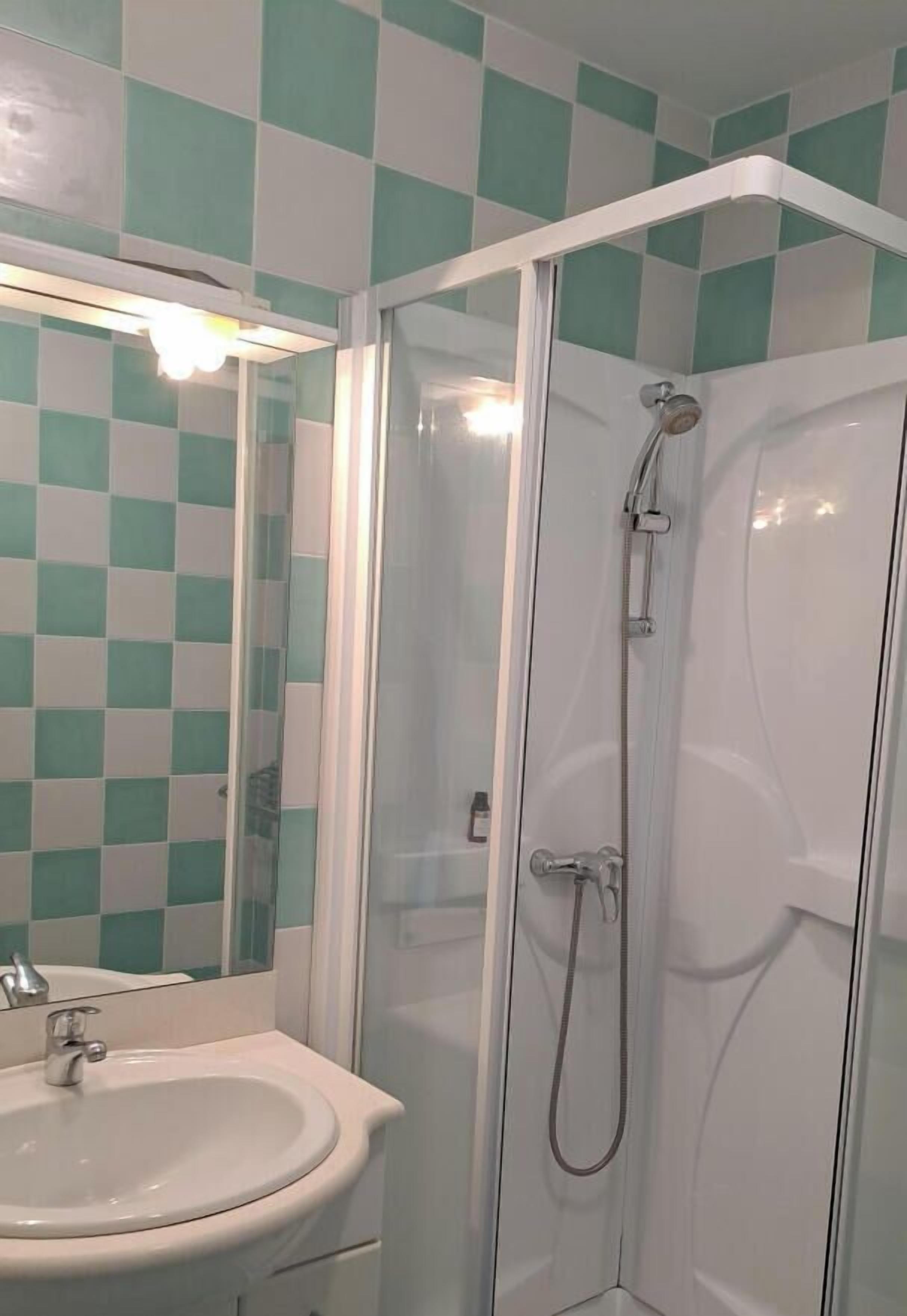 A bathroom with a checkered tile wall, a white sink, and a glass-enclosed shower.