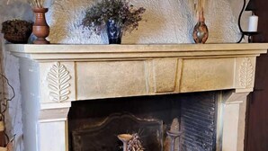 A fireplace with a textured mantel, a small shelf with decorative items, and a tiled floor. - Fraissines at Myriam and Laurent's (FRAISSINES)