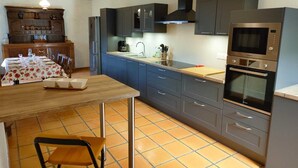 A modern kitchen with grey cabinets, a wooden dining table, and a built-in oven. - Fraissines at Myriam and Laurent's (FRAISSINES)