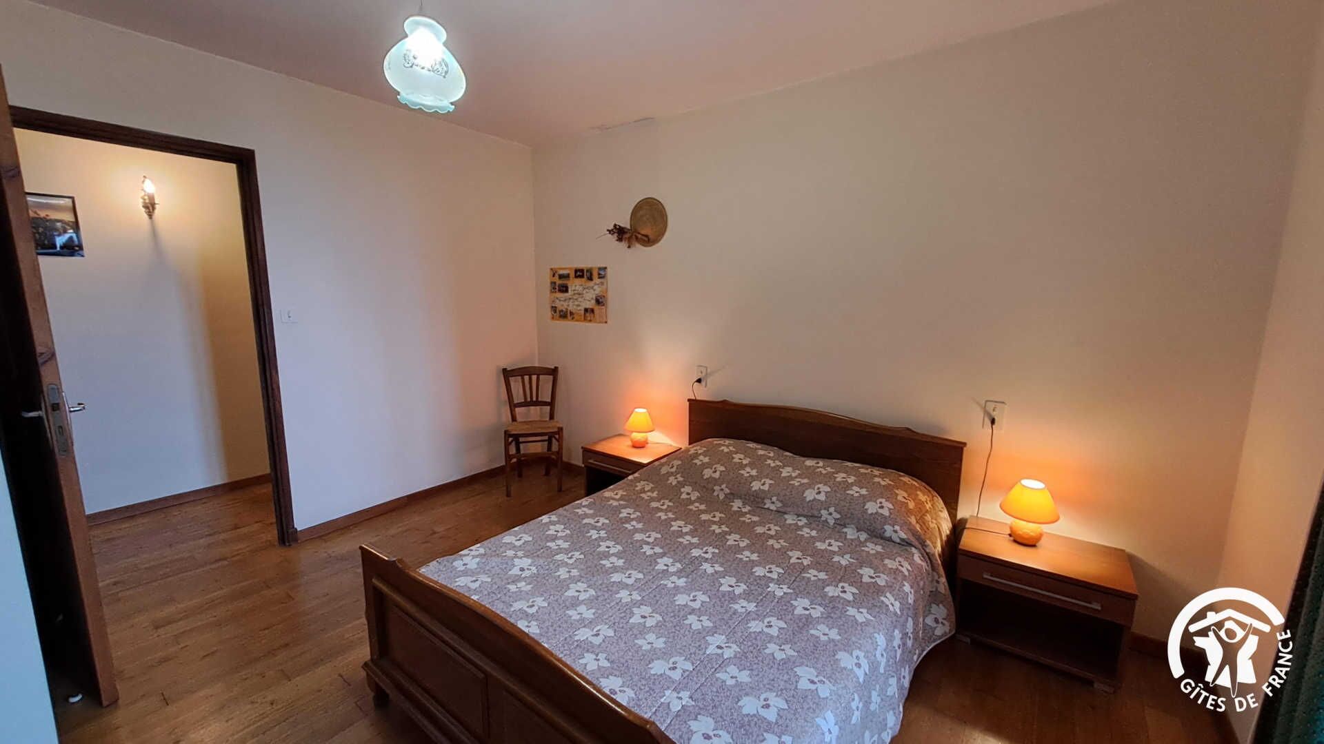 Une chambre à coucher avec un lit en bois, deux lampes de chevet, une chaise et un luminaire fixé au mur.