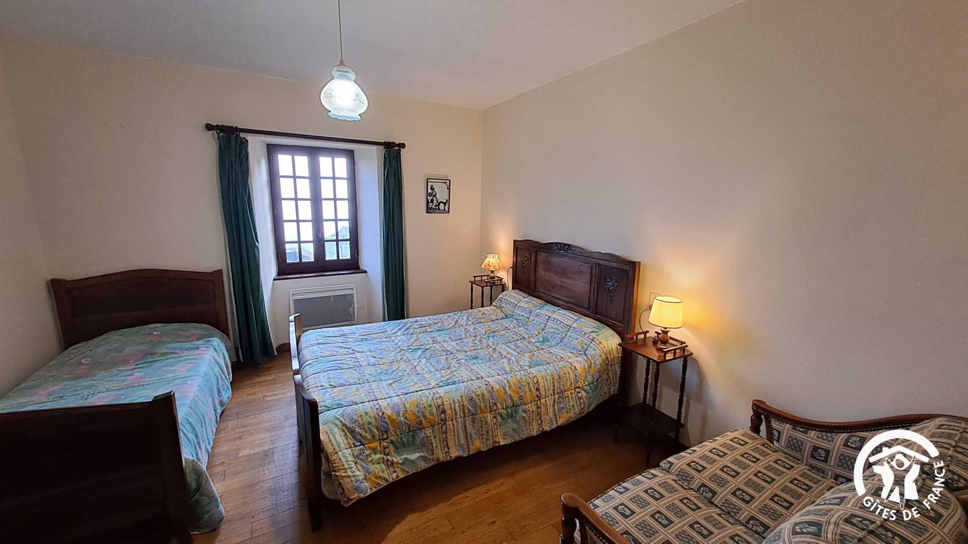 Ein Schlafzimmer mit zwei Einzelbetten, einem großen Bett, einem Fenster mit Vorhängen, einem Heizkörper und einem an der Wand hängenden Bild.