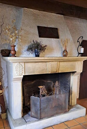 A fireplace with a textured mantel, a small shelf with decorative items, and a tiled floor.