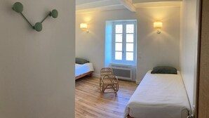 A bedroom with two beds, a wicker chair, and two wall-mounted lamps.