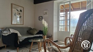 A cozy living room with a sofa, a glass coffee table, and a wicker chair. There is a window with a view of the outdoors.