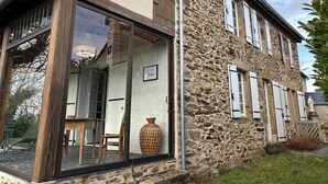 A stone building with a large glass door and windows, a wooden table, and a large vase.