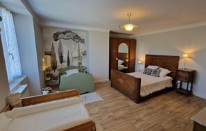 A bedroom with a bed, a chair, a mirror, and a wooden floor.