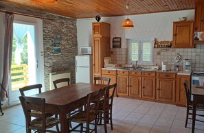 A kitchen with wooden cabinets, a dining table with chairs, a refrigerator, a microwave, and a stove.
