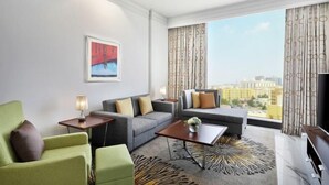 A modern hotel room with a sofa, armchair, coffee table, and a large window with curtains.