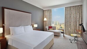 A hotel room with a large bed, a desk, a chair, a sofa, and a view of the city.