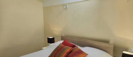 A bedroom with a bed, two bedside lamps, a skylight, and a nightstand with a lamp.