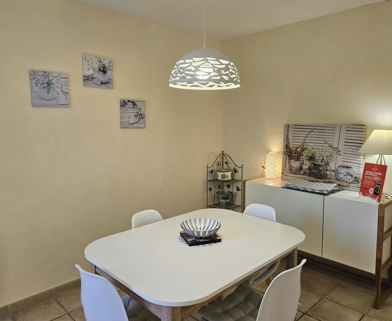 A dining area with a white table, chairs, and a hanging light fixture.
