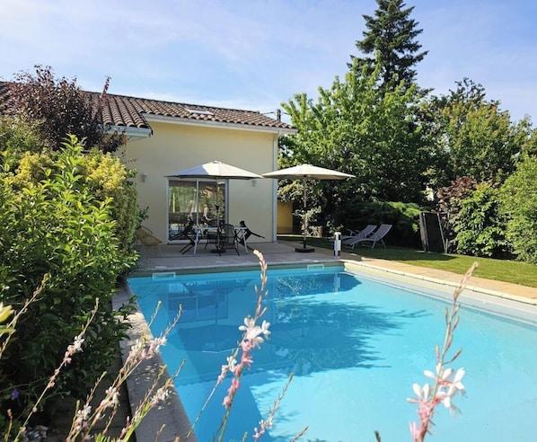 A swimming pool with a patio area, surrounded by greenery and a building with a tiled roof. - Les Perdrix - GAILLAC (GAILLAC)