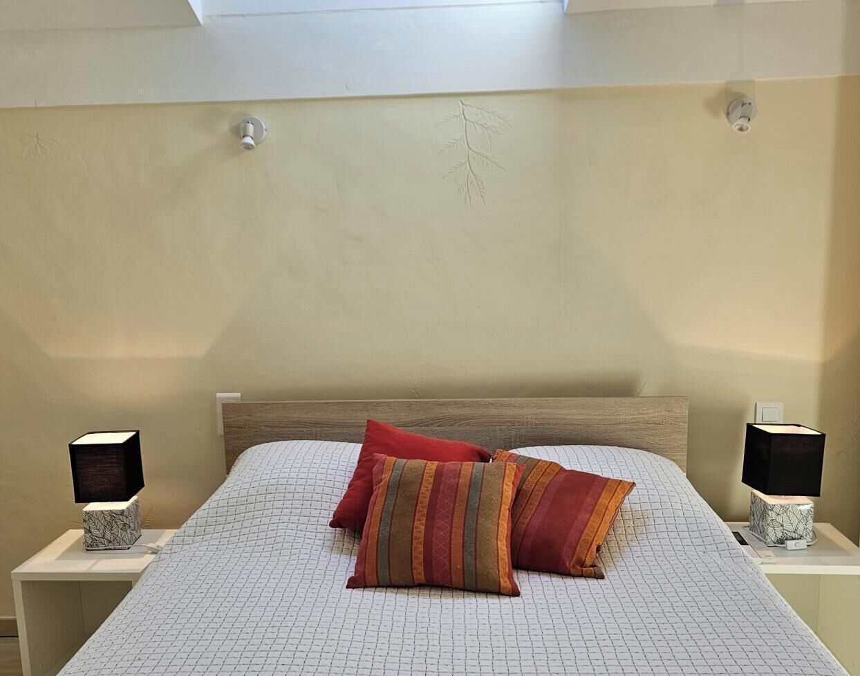 A bedroom with a bed, two bedside tables, and two wall-mounted lamps.