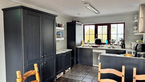 A kitchen with dark cabinets, a central island, a window with a view, and a stone-tiled floor. - Brú na Dromoda Dromid Hostel (Killeenleagh)
