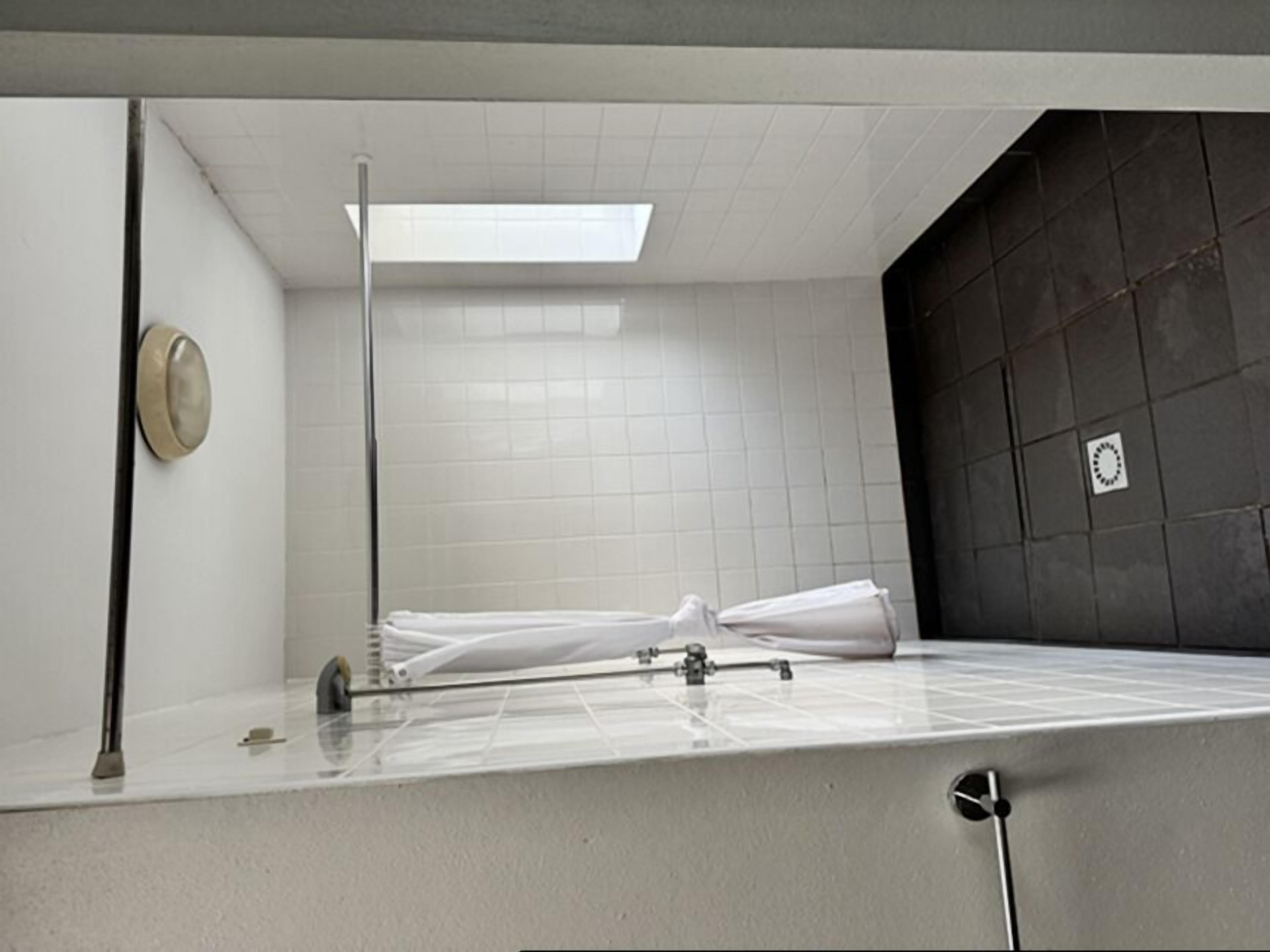 A small, tiled shower room with a white shower curtain rod and a single showerhead.