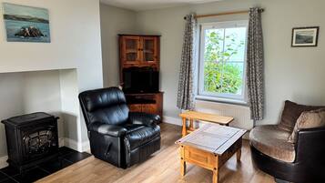 A living room with a black leather sofa, a wooden coffee table, a black leather armchair, a wooden cabinet, and a black wood-burning stove.