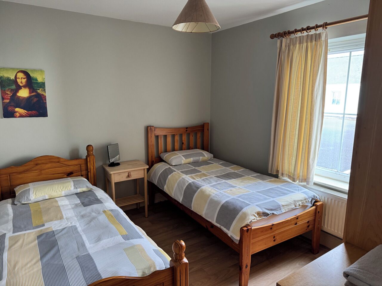 Camera da letto con due letti di legno, un comodino, una lampada e una finestra con tende.