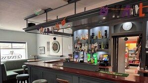 A bar area with stools, a dartboard, and shelves of bottles. - Brú na Dromoda Dromid Hostel (Killeenleagh)
