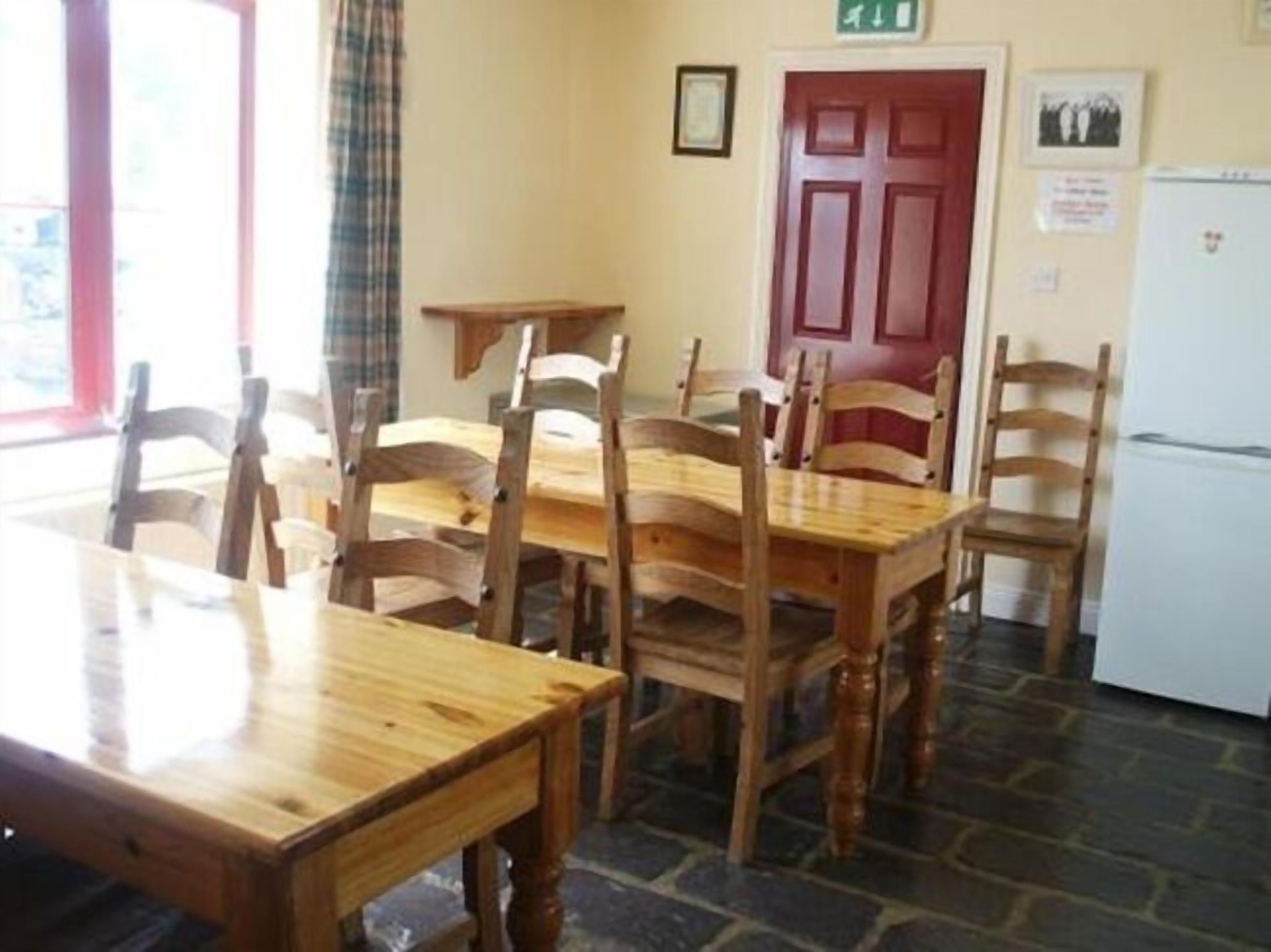 Un coin repas avec des tables et des chaises en bois, une porte rouge et un réfrigérateur.