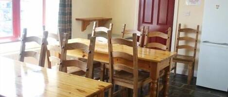 Un coin repas avec des tables et des chaises en bois, une porte rouge et un réfrigérateur.