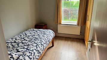 A bedroom with a bed, a radiator, a window with curtains, and a door.