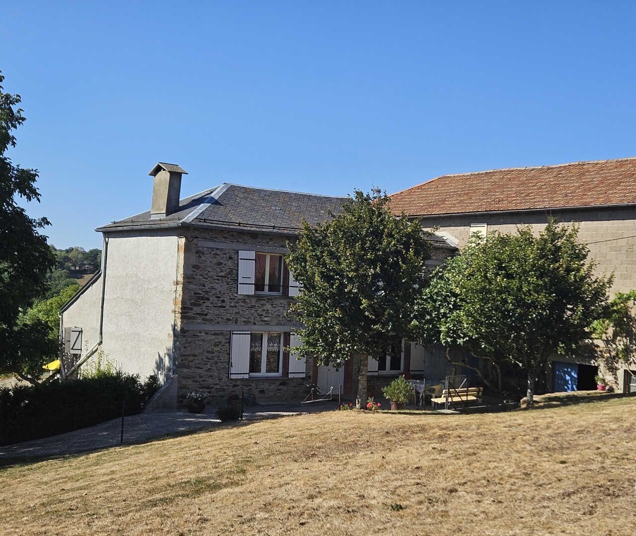 A stone house with a tiled roof, a small garden, and a clear blue sky.