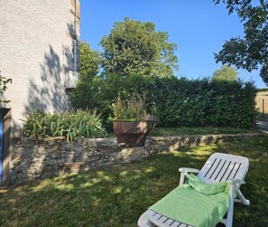 A white lounge chair with a green cover, a large potted plant, and a stone wall.