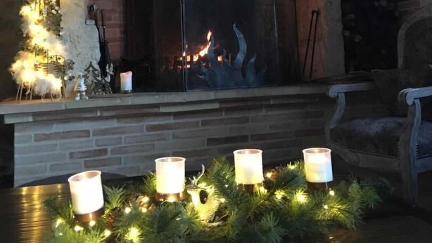 Una chimenea con una decoración de cráneo de ciervo, fuego encendido y un árbol de Navidad con luces y velas.